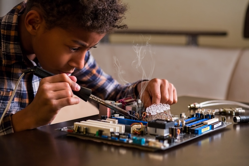 Boy in concentration, fixing a motherboard with soldering tool.