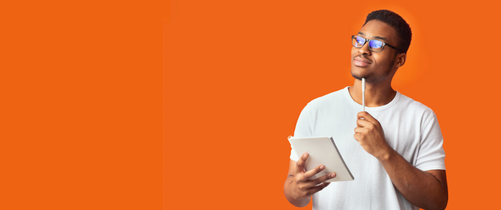 orange banner image of young man holding a pen and a notebook, looking up pensively.