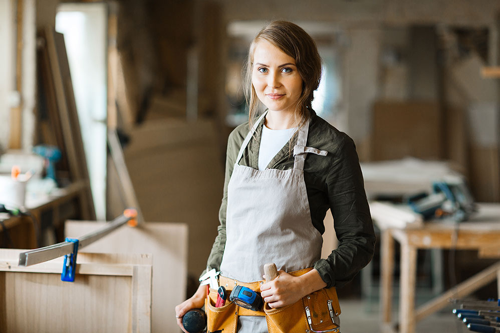 woman in coveralls and toolbelt smiling at camera.